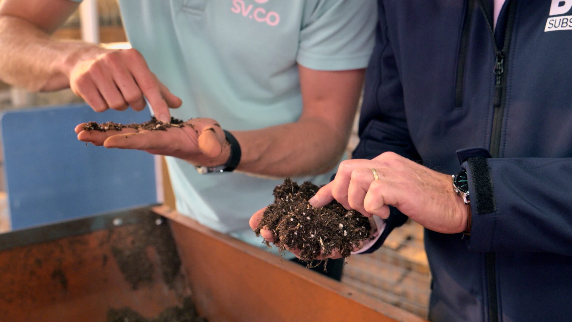 Twee personen bekijken en vergelijken handvol substraat, waarbij de structuur van het reed canary grass mengsel zichtbaar wordt.